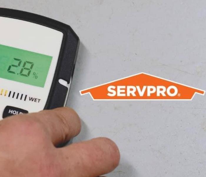 A hand is shown holding a moisture detecting monitor to a wall, a SERVPRO orange logo is shown.